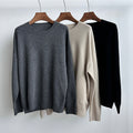 Three sweaters in gray, beige, and black on wooden hangers against a white background