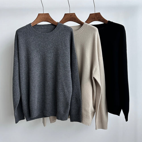 Three sweaters in gray, beige, and black on wooden hangers against a white background
