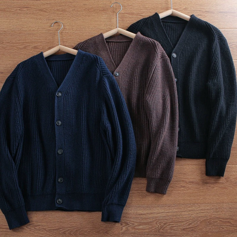 Three cardigans in navy, brown, and black hanging on a wooden surface.