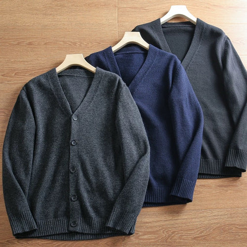 Three cardigans in gray, navy, and black on hangers against a wooden background